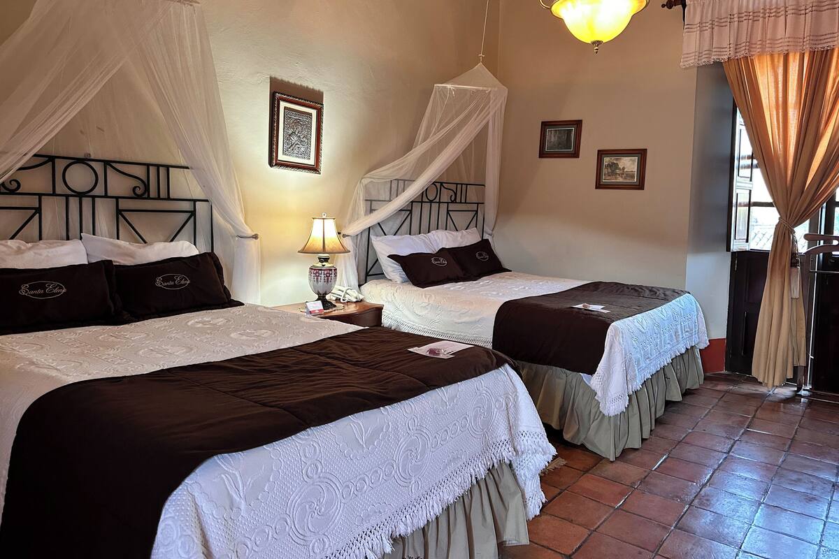 Une chambre avec deux lits, une table de chevet avec une lampe, un lit à baldaquin et un lustre.