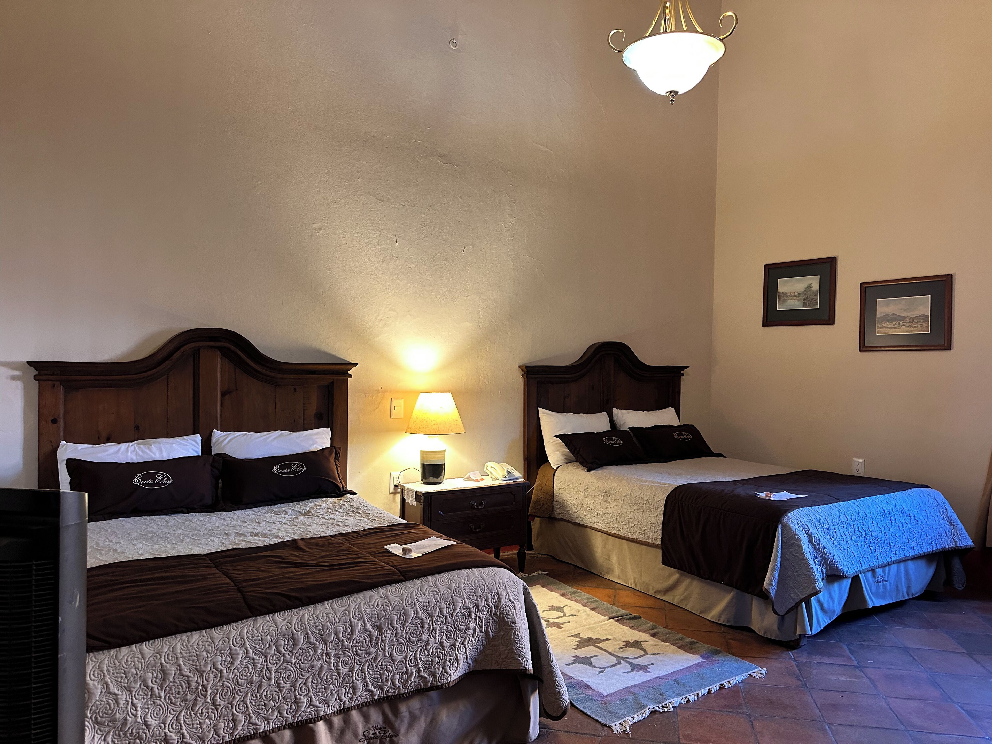 Une chambre double avec deux lits, chacun doté d’une tête de lit en bois, d’une table de chevet avec une lampe et d’un tapis sur le sol.