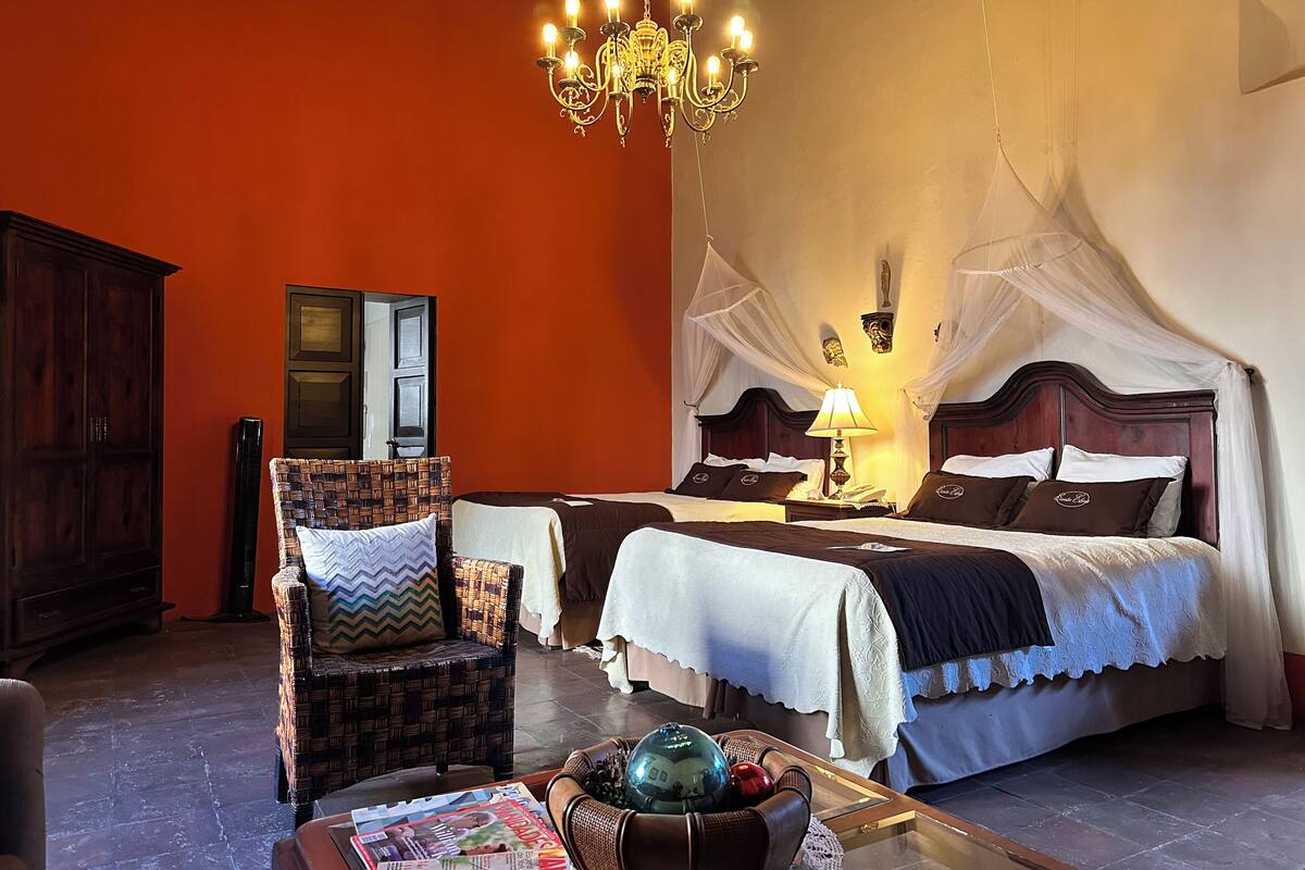 Une chambre à coucher avec un grand lit, une chaise, une table avec des magazines et un lustre.