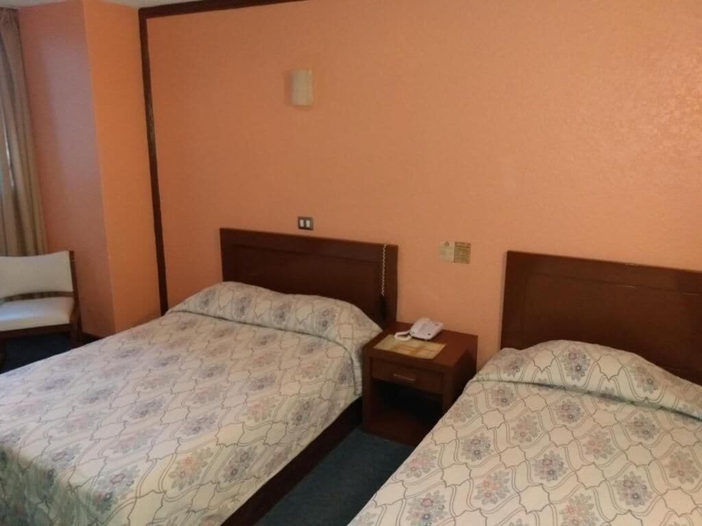 Una habitación de hotel con dos camas, una mesita de noche con teléfono y una silla.