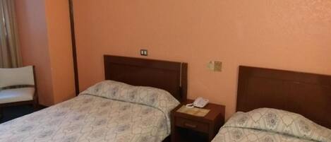 Una habitación de hotel con dos camas, una mesita de noche con teléfono y una silla.