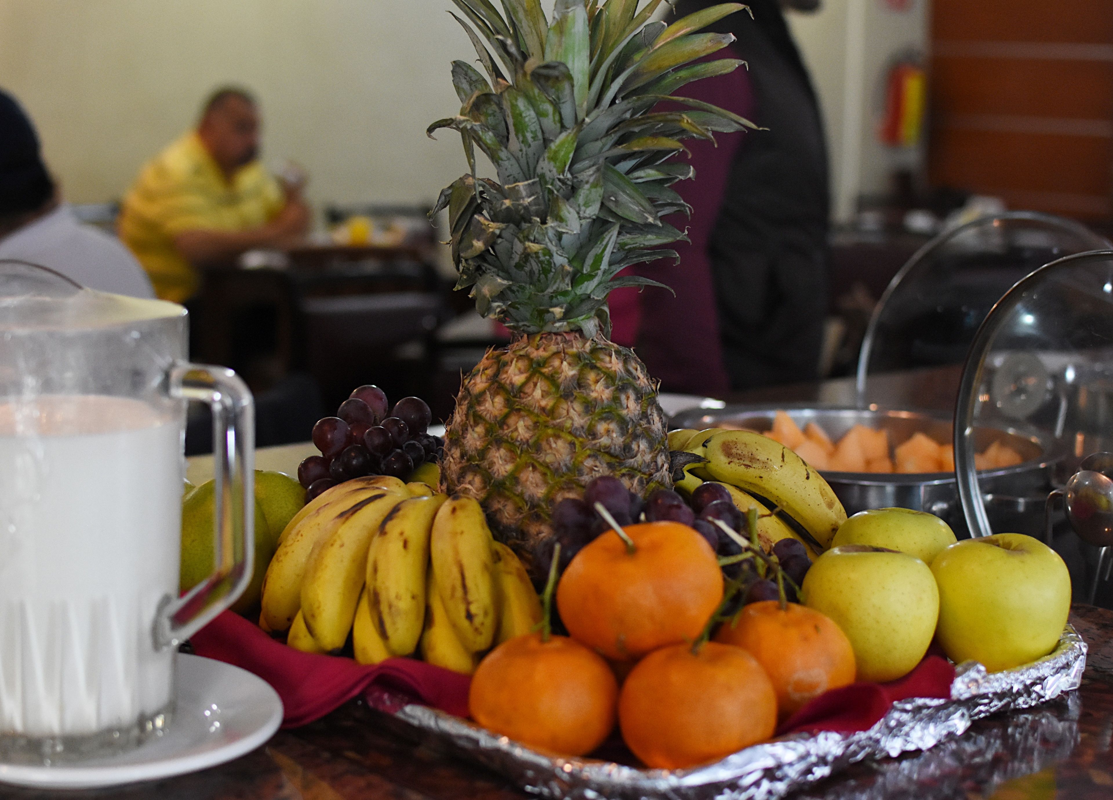 Una bandeja de frutas con piña, plátanos, uvas, naranjas y manzanas sobre una mesa.
