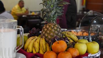 Una bandeja de frutas con piña, plátanos, uvas, naranjas y manzanas sobre una mesa.