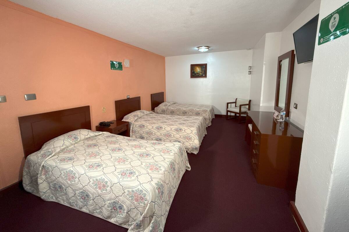 A hotel room with two beds, a desk, a chair, a mirror, and a painting on the wall.