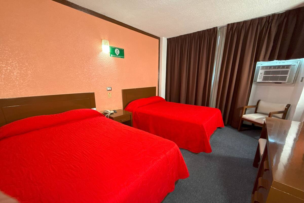 A hotel room with two beds, a desk, a chair, an air conditioning unit, and a curtain.