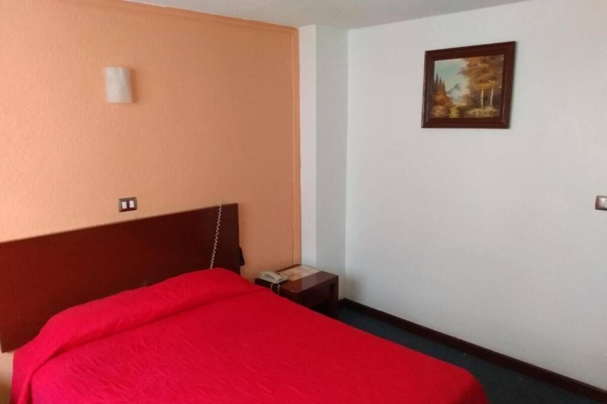 A hotel room with a bed, a nightstand, a telephone, and a painting on the wall.