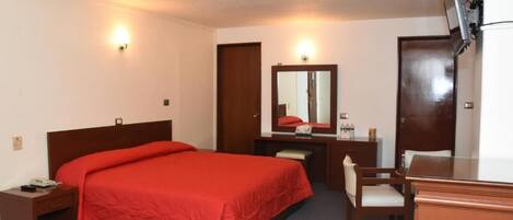 Habitación de hotel con una cama individual, un escritorio, una silla, un espejo y un televisor fijado a la pared.