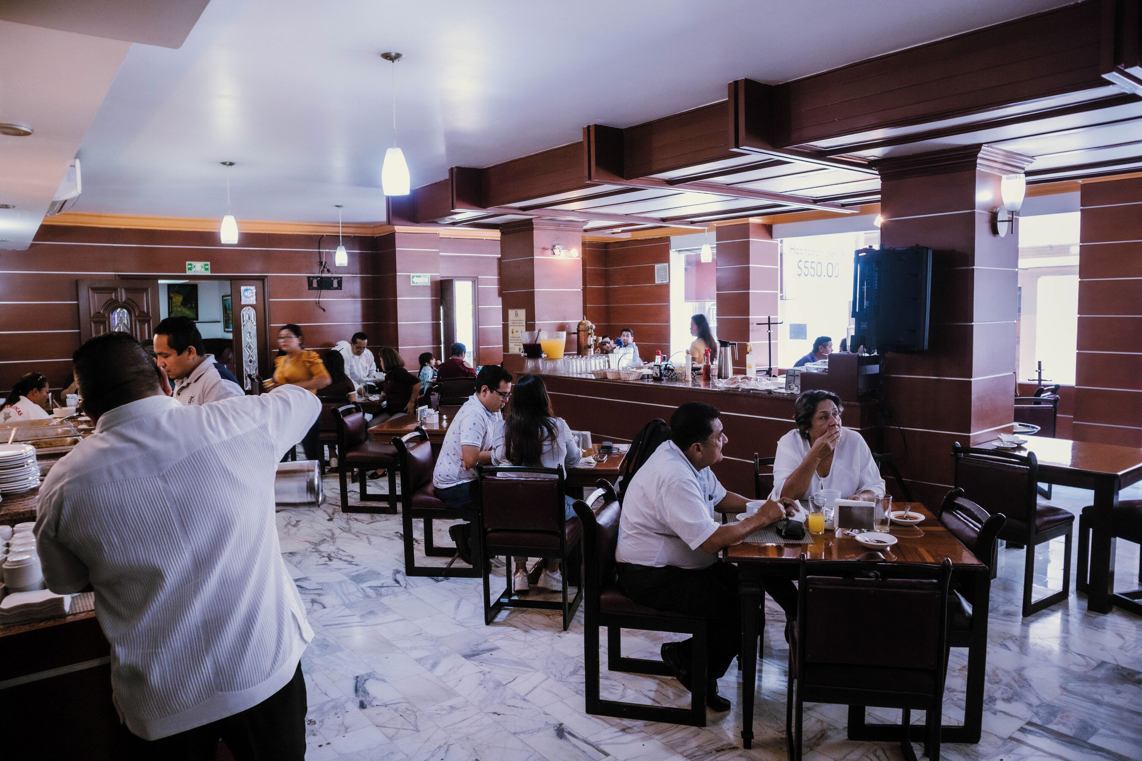 A spacious restaurant with marble flooring and wooden paneling, featuring multiple dining tables and chairs.