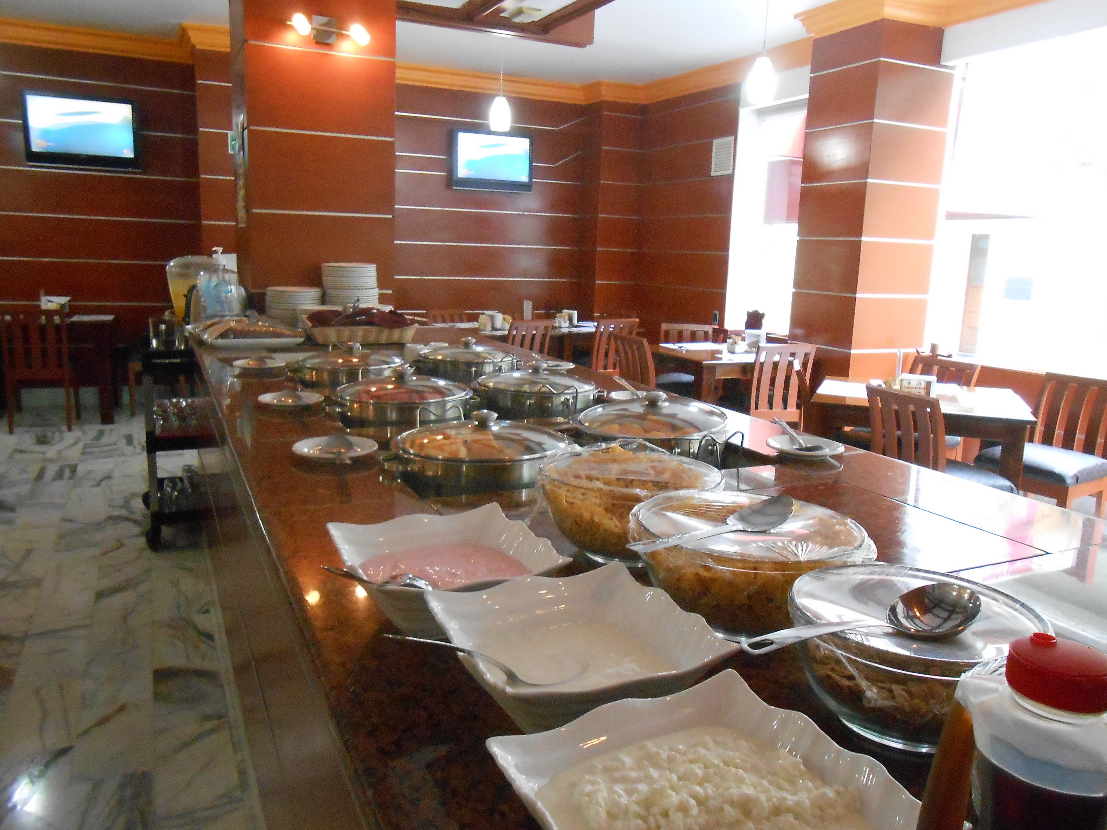 A buffet setup with various food items and utensils on a long table, surrounded by chairs and tables in a dining area with wooden walls and ceiling.