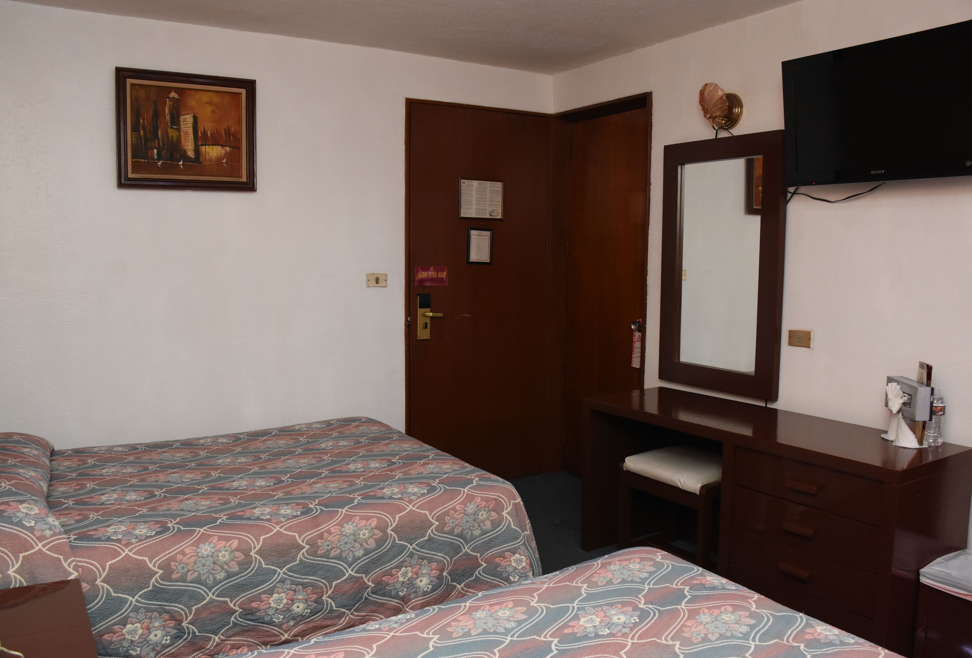 A hotel room with two beds, a desk, a chair, a dresser, a television, and a painting on the wall.