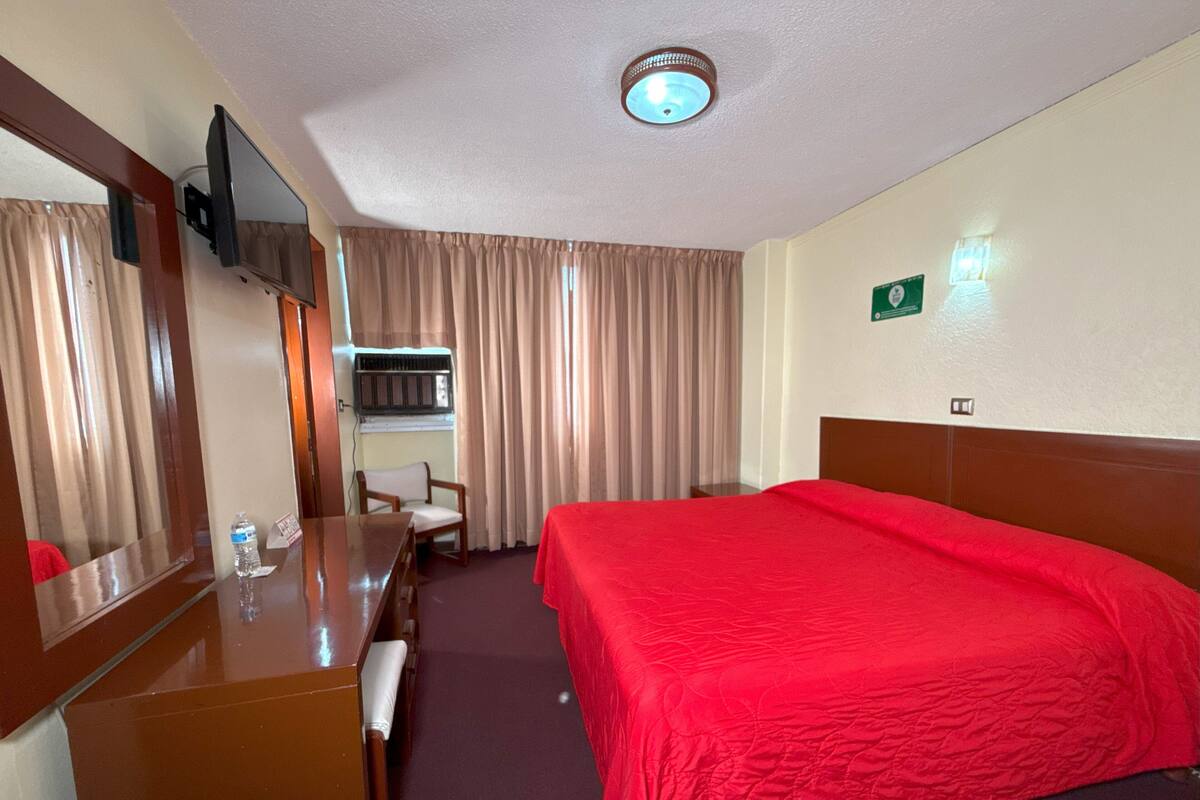 A hotel room with a bed, a desk, a chair, a television, and a mirror.