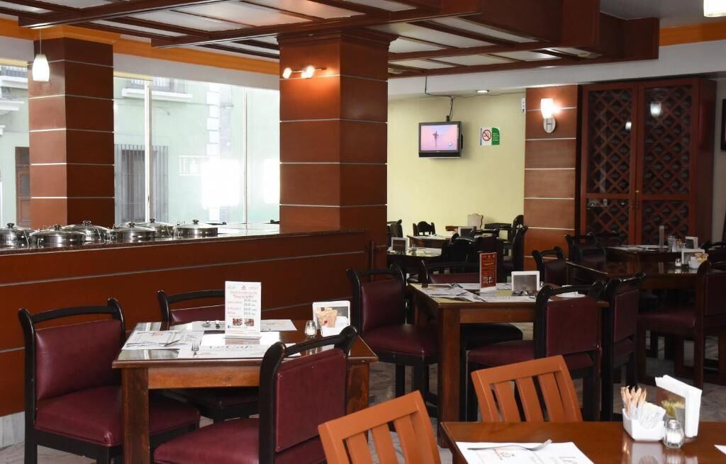 Un restaurante con mesas y sillas de madera, una zona de buffet con ollas, y un televisor en la pared.
