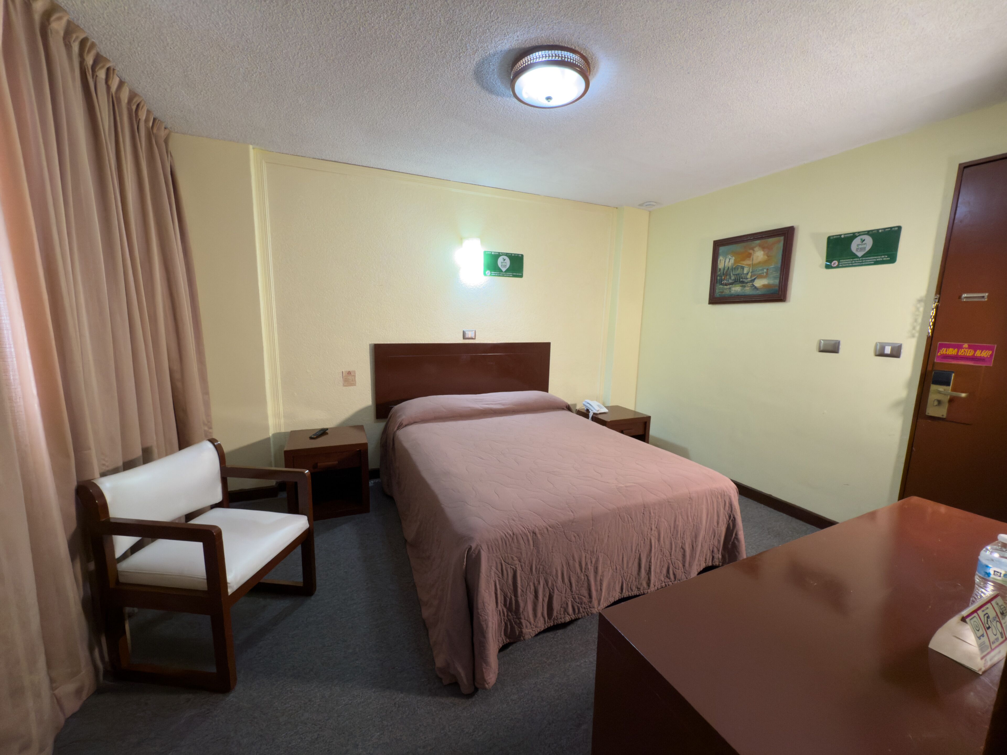 A hotel room with a bed, a chair, a desk, a nightstand, and a door.