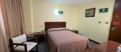 A hotel room with a bed, a chair, a desk, a nightstand, and a door.