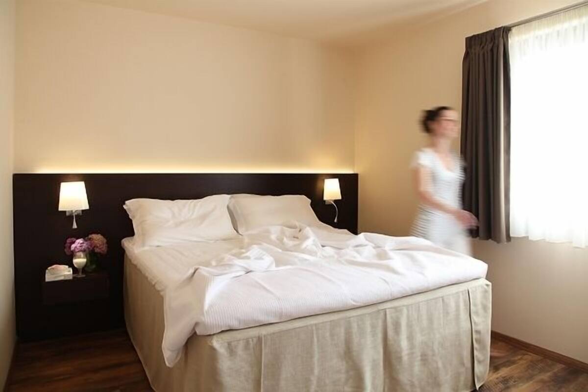 Quarto de hotel com cama bem arrumada, luminárias de cabeceira e mesa de cabeceira com um vaso de flores.