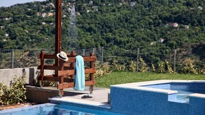 Piscina con un banco de madera y un sombrero, rodeada por una valla y follaje.