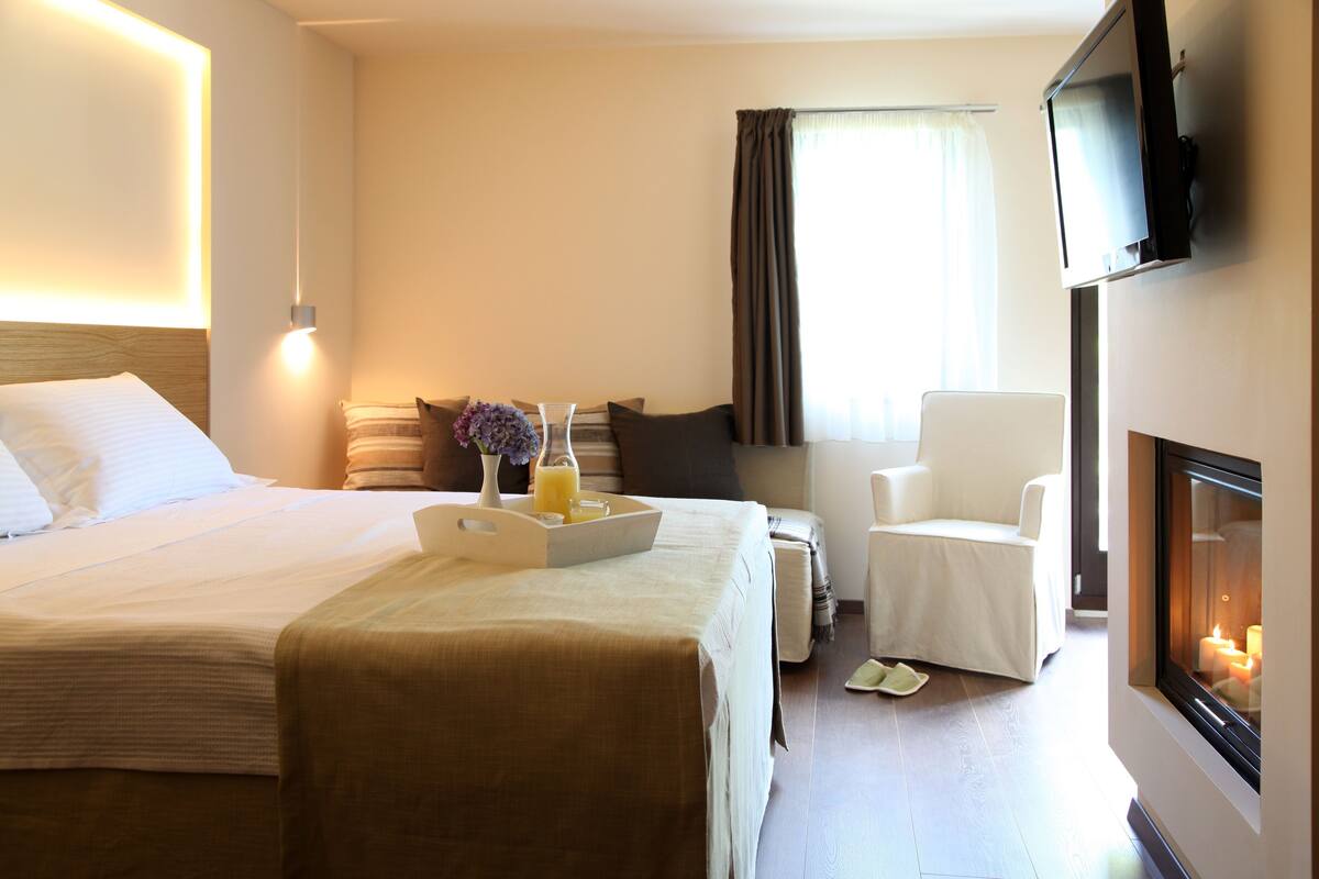 Quarto de hotel com cama, mesa de cabeceira com bandeja de itens de café da manhã, uma cadeira, televisão e lareira.