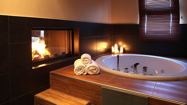 Un baño moderno con suelo de madera, una bañera grande y una chimenea.