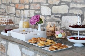 A breakfast buffet with pastries, fruits, and beverages on a stone wall backdrop. - Theta Hotel (Zagora-Mouresi)