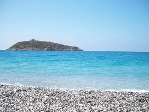 A pebbly beach with clear turquoise water and a small rocky island in the distance. - Hotel San Gaetano (Grisolia)