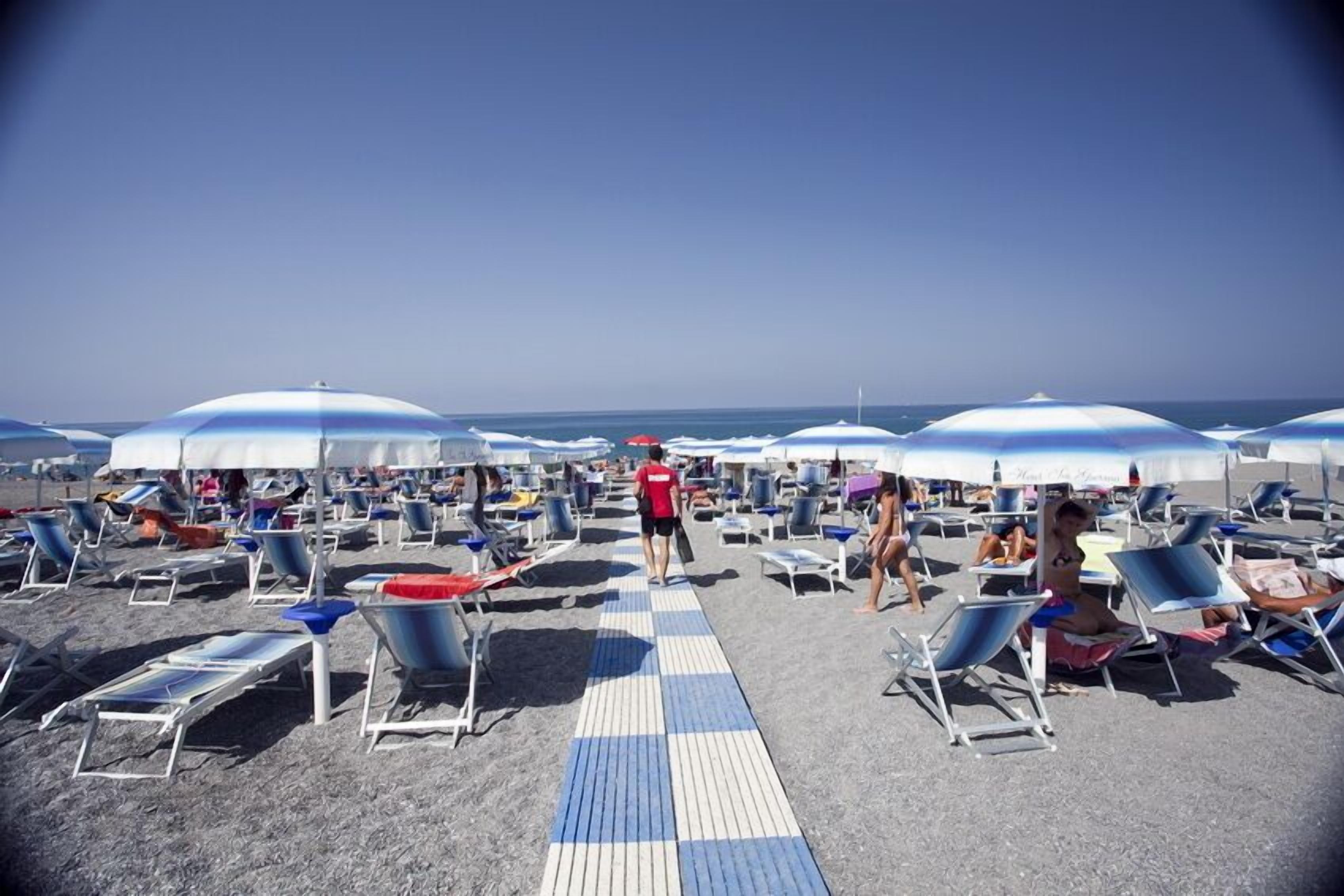 Une plage bordée de rangées de chaises longues et de parasols, un ciel dégagé et une personne qui se promène.