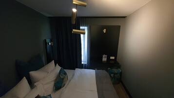 A modern hotel room with a large bed, a bedside table, a lamp, and a view of the outdoors.