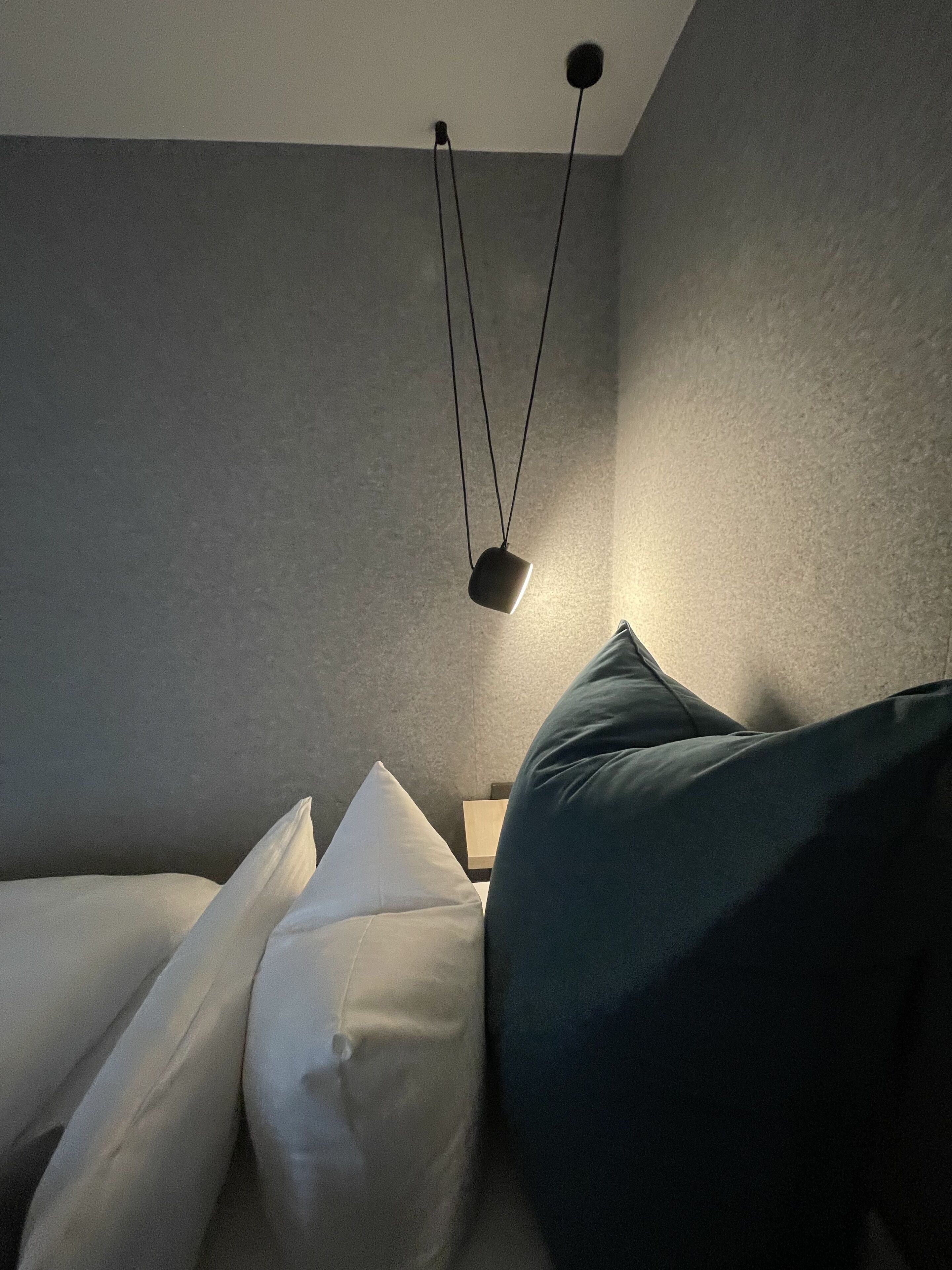 Una habitación con una cama, almohadas y una lámpara colgante.