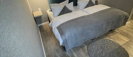 A modern bedroom with a bed, bedside tables, a blue chair, and a round rug.