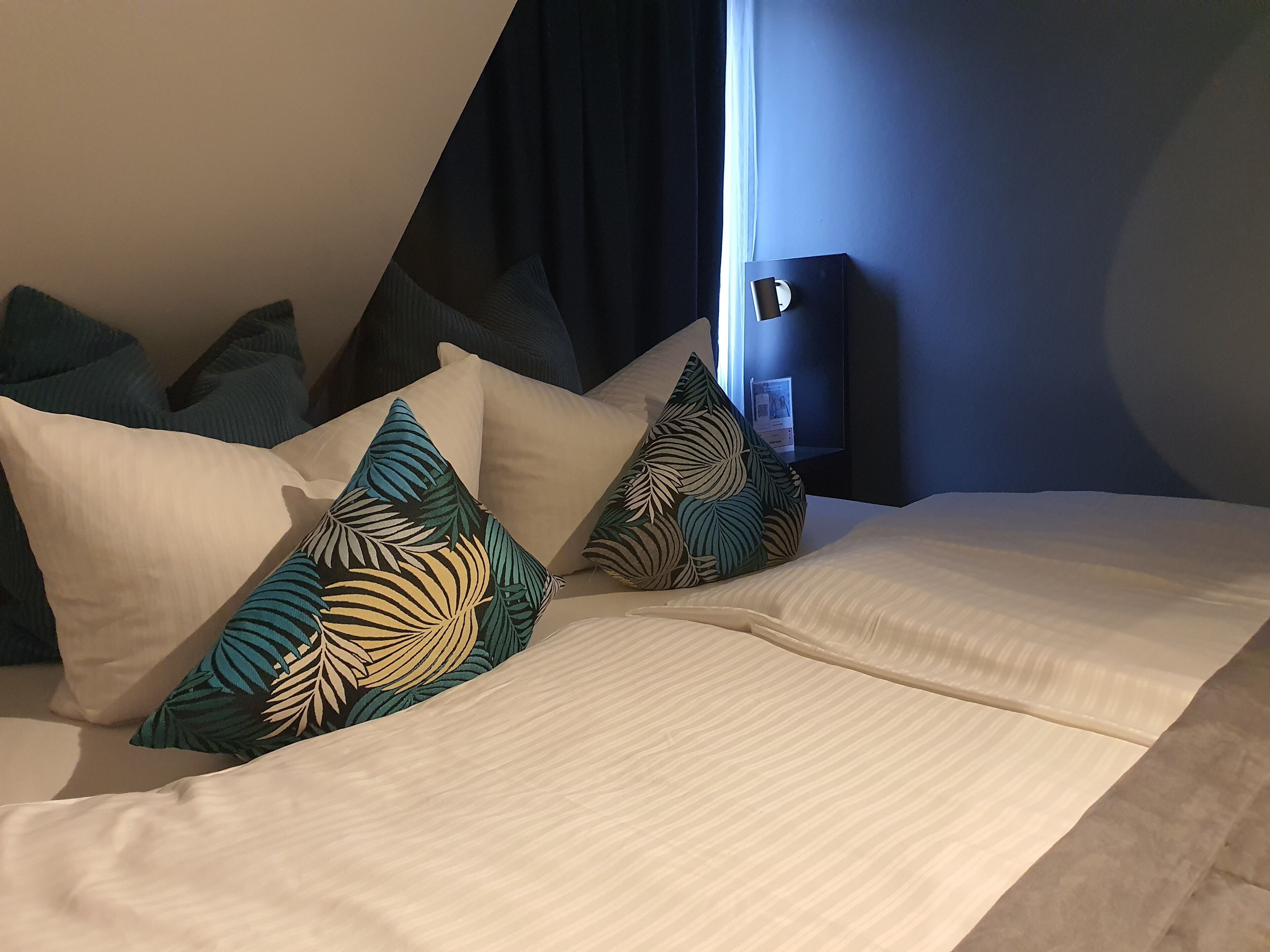 A neatly made bed with a white bedspread and several pillows with tropical leaf patterns.