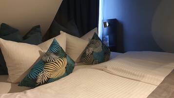 A neatly made bed with a white bedspread and several pillows with tropical leaf patterns.