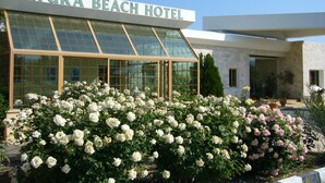 L’extérieur de l’hôtel Natura Beach se distingue par sa grande façade vitrée et le jardin de roses blanches et roses qui s’étend devant l’entrée.