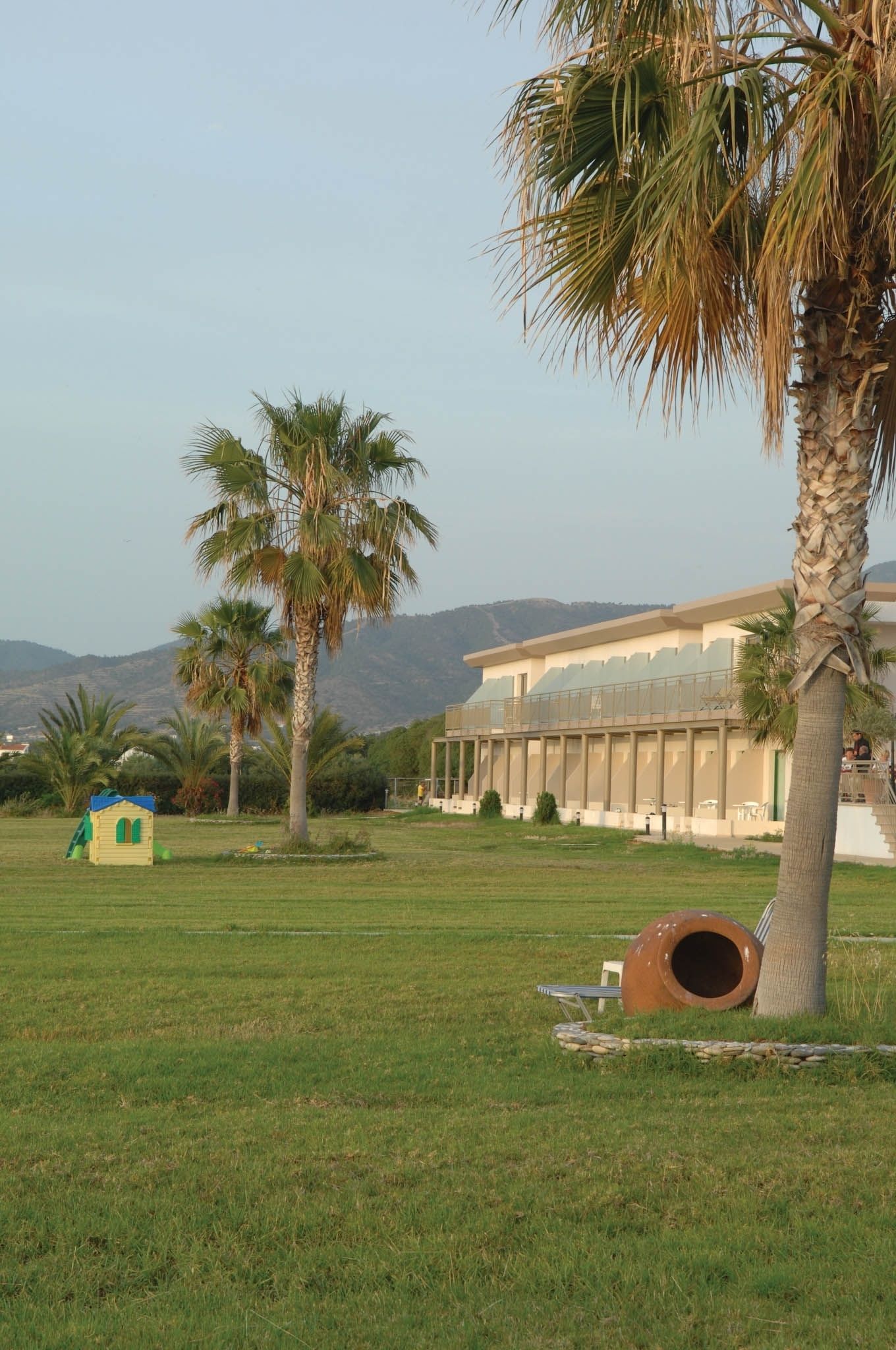 A building with a flat roof and large windows, surrounded by palm trees and a grassy field.