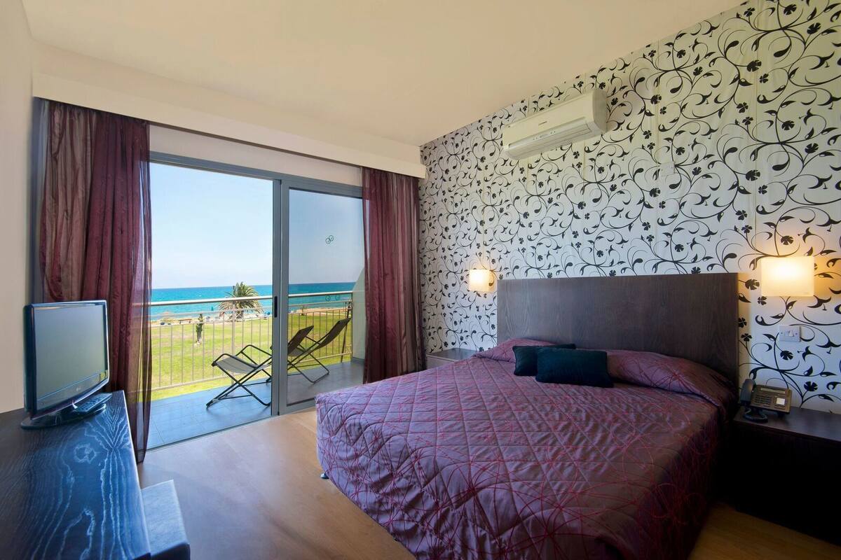 Une chambre d’hôtel avec un lit, une télévision, un balcon donnant sur la mer et un mur décoré de motifs.