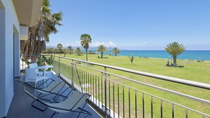 Un balcon avec vue sur la mer, des chaises blanches et un palmier.