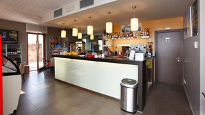 A modern bar area with a central counter, hanging pendant lights, and a variety of bottles and glasses on shelves. - Hotel Lido (Torri del Benaco)