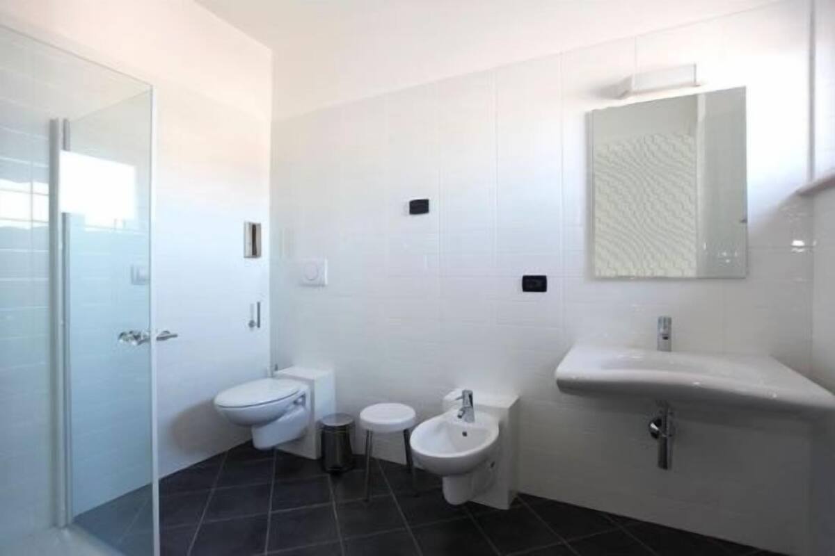 A modern bathroom with a toilet, bidet, sink, and glass shower enclosure.
