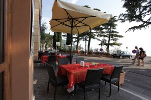 Un espace extérieur aménagé pour les repas, avec des tables et des chaises, un grand parasol et des plantes en pot.