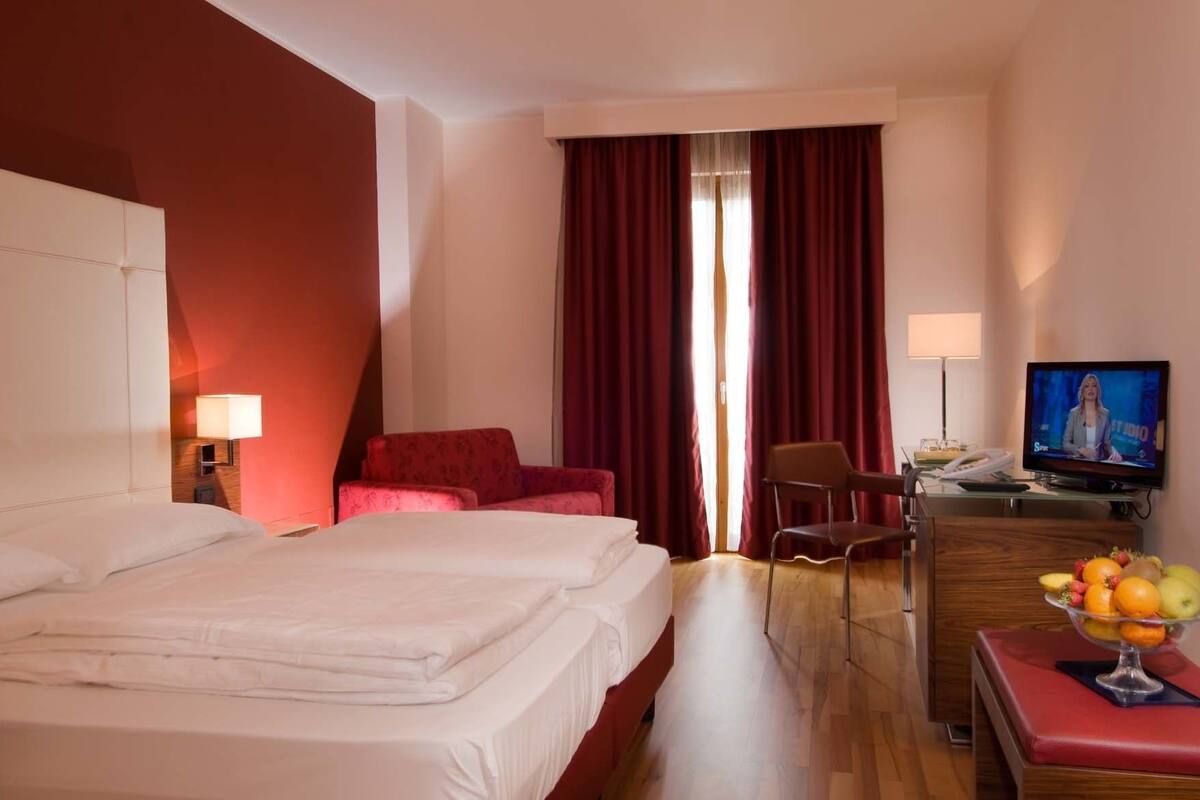 A hotel room with two beds, a desk, a television, and a fruit bowl.