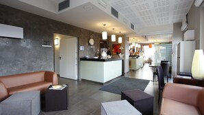 A modern hotel lobby with a reception desk, seating area, and a kitchen in the background. - Hotel Lido (Torri del Benaco)