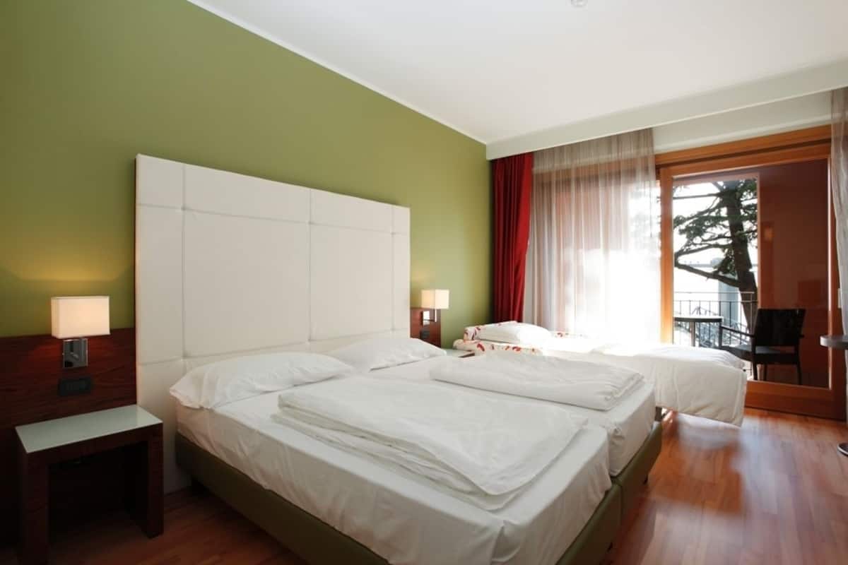 A hotel room with two beds, a wooden nightstand, a lamp, and a view of the outdoors.