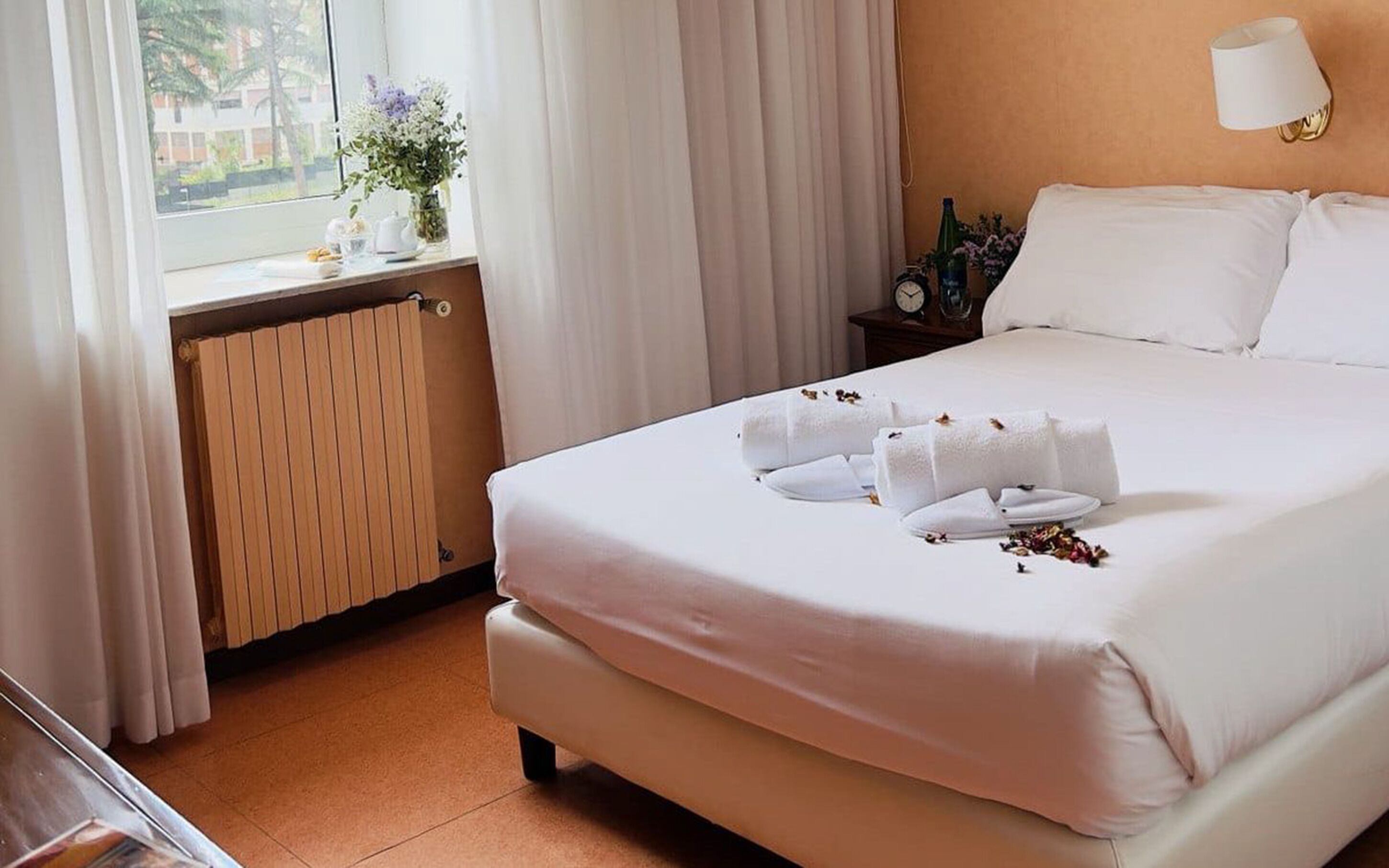 A hotel room with a large bed, a bedside table with a lamp, a window with curtains, and a view of the outside.