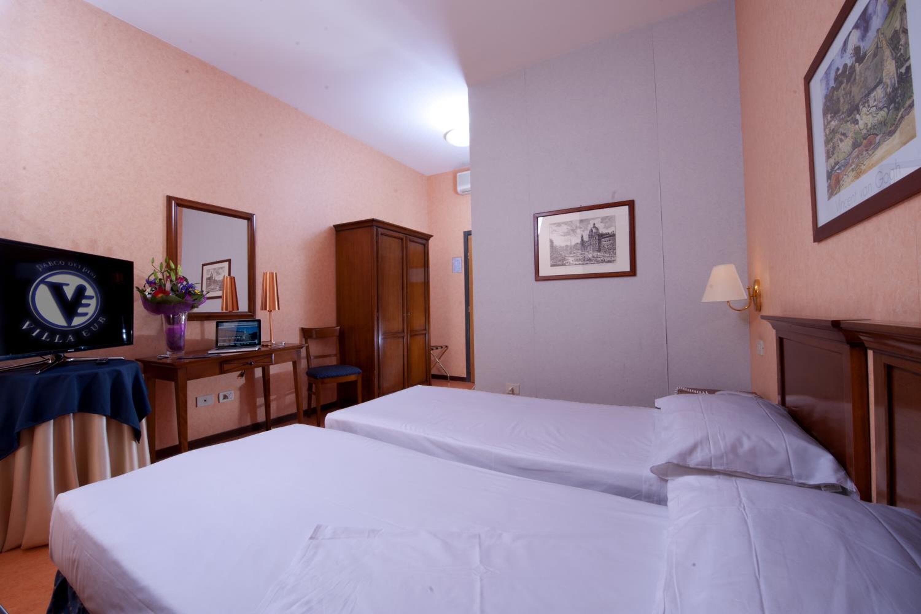 A hotel room with two beds, a desk with a computer, a TV, and a mirror.