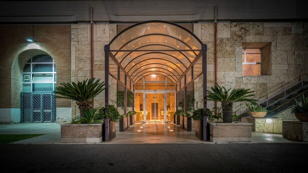 A modern building entrance with a glass canopy, brick walls, and potted plants. - Villa EUR - Parco dei Pini (Rome)