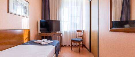 A hotel room with a bed, a desk with a television, a chair, and a large mirror.
