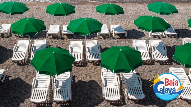 Ein Strand mit Reihen weißer Liegestühle und grüner Sonnenschirme, ein klares blaues Meer und ein Logo unten rechts.