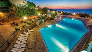 Ein Pool mit Liegestühlen und einem Kiesweg, umgeben von Grün und Blick aufs Meer.