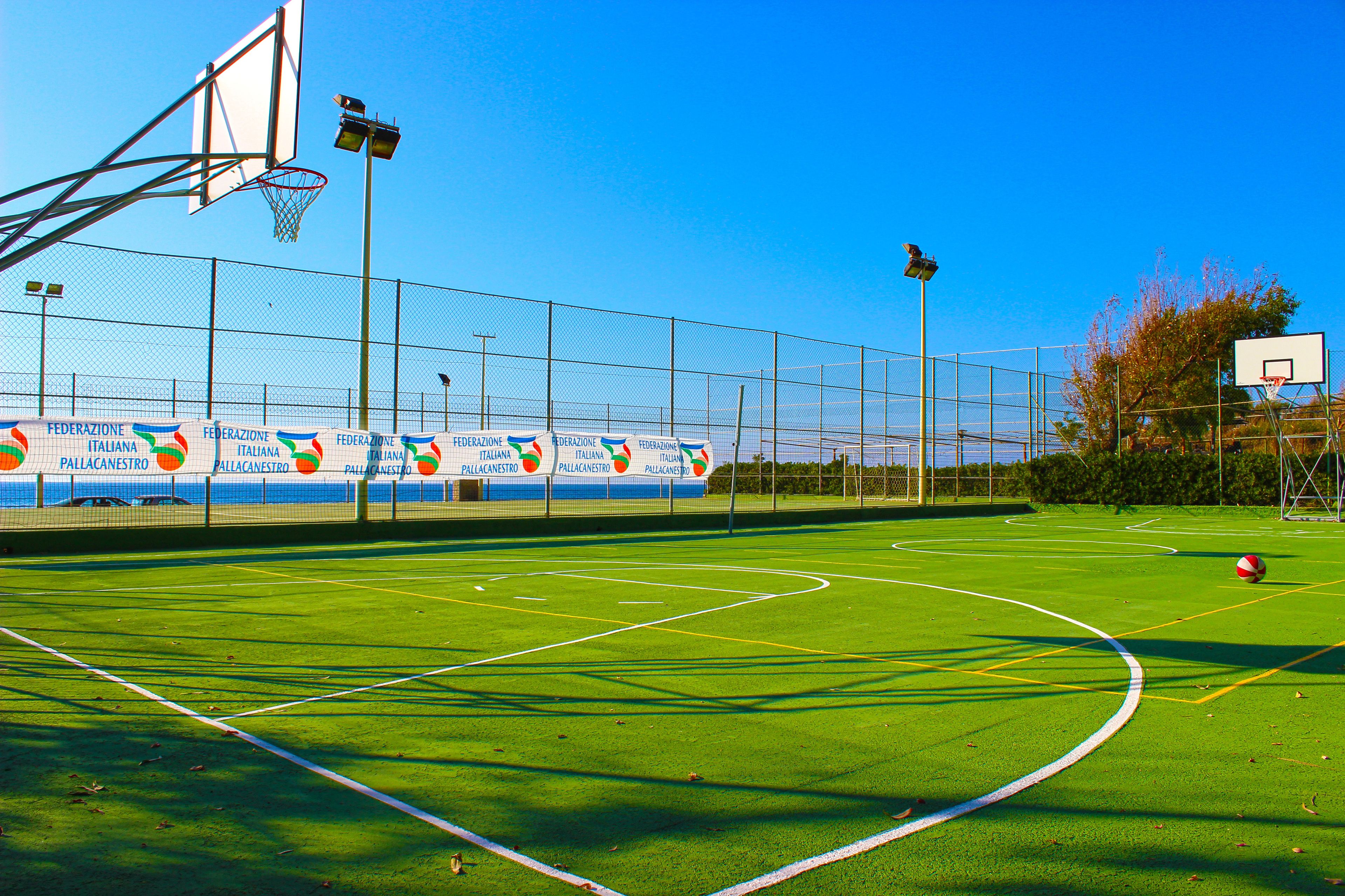 An outdoor basketball court with a clear sky, surrounded by a fence, and banners along the fence.