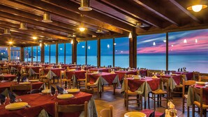 Ein Restaurant mit mehreren gedeckten Tischen, großen Fenstern mit Meerblick und einer Holzzahlendele mit hängenden Lampen.