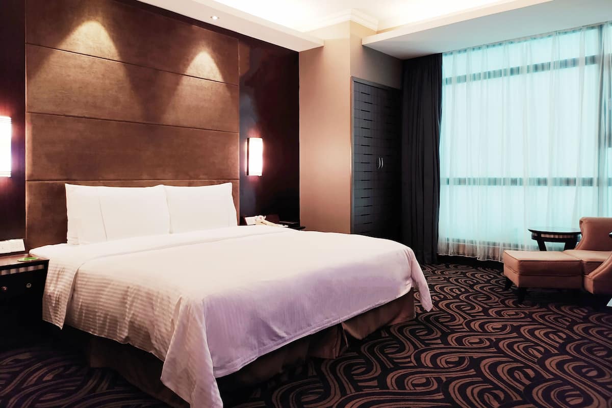 Una habitación de hotel con una cama grande, una mesita de noche, una silla, un armario y una ventana con cortinas.