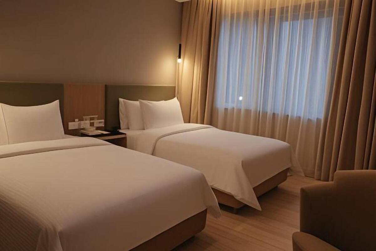 A hotel room with two beds, a nightstand, a chair, and a large window with curtains.